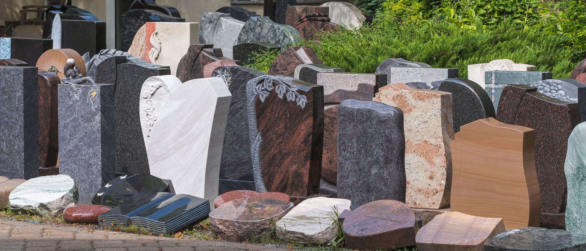 Eine Reihe von steinernen Grabsteinen auf einem Friedhof, umgeben von Gras und kleinen Pflanzen.